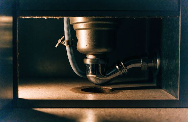 Garbage disposal mounted under a kitchen sink with its discharge tube running to the trap