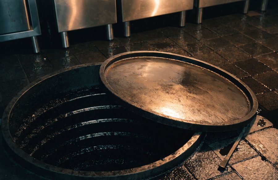 Commercial kitchen grease interceptor with the heavy lid lifted, showing the baffled chamber below