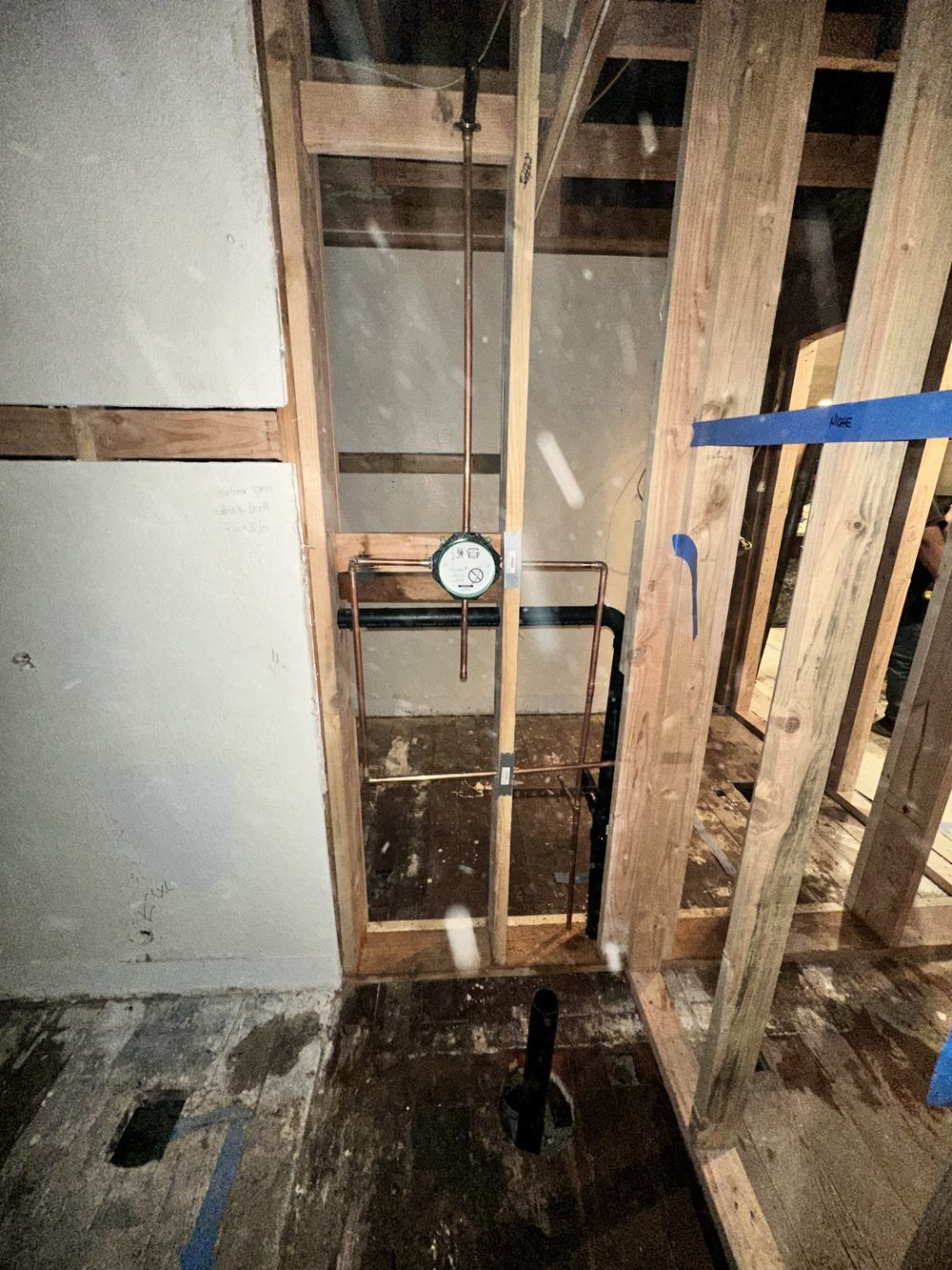 New copper water lines and black ABS drain piping run through open floor framing during a repipe, with a gauge mounted on the run